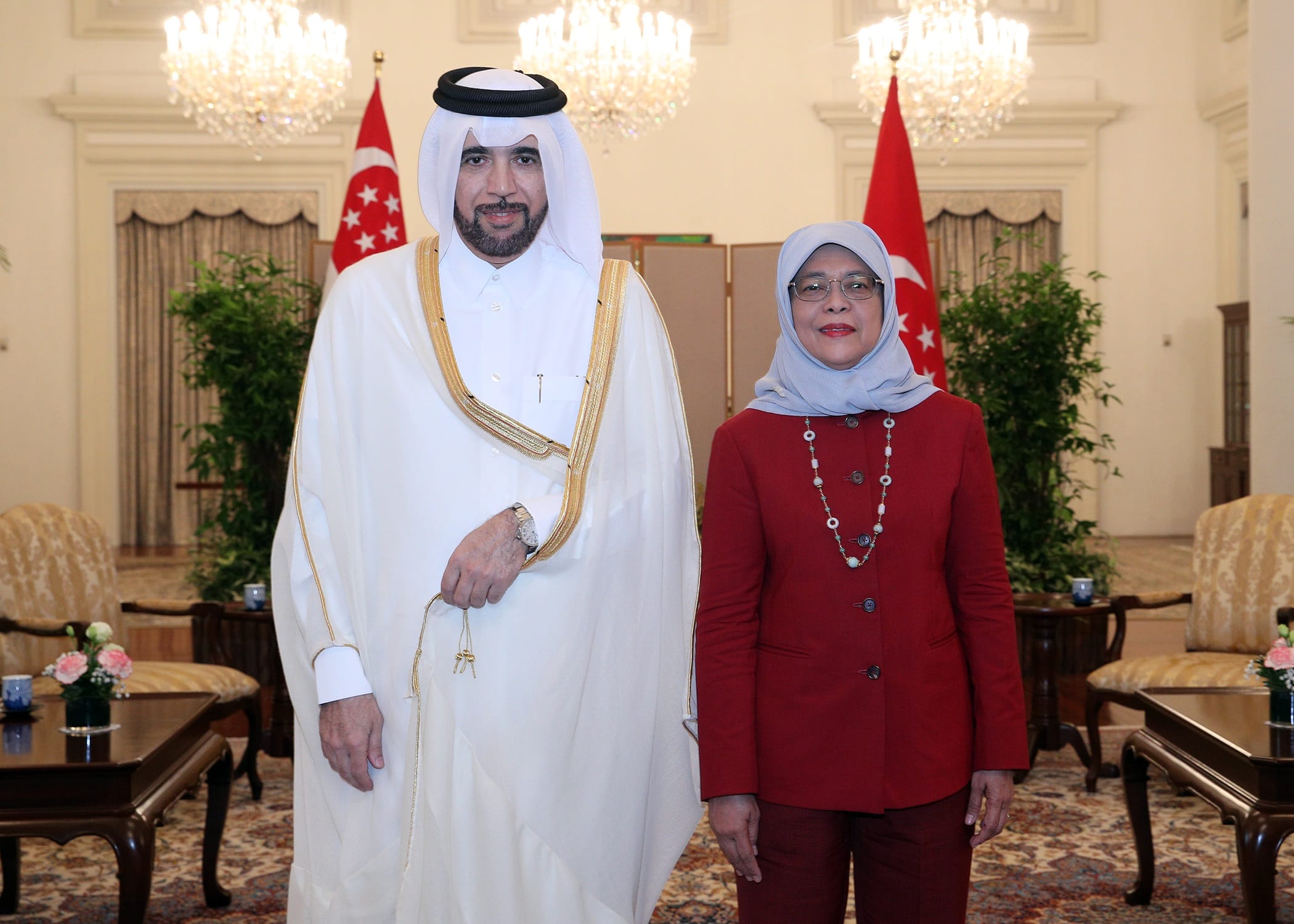 Halimah Yacob and Qatari official pose indoors with Singapore flags and chandeliers.